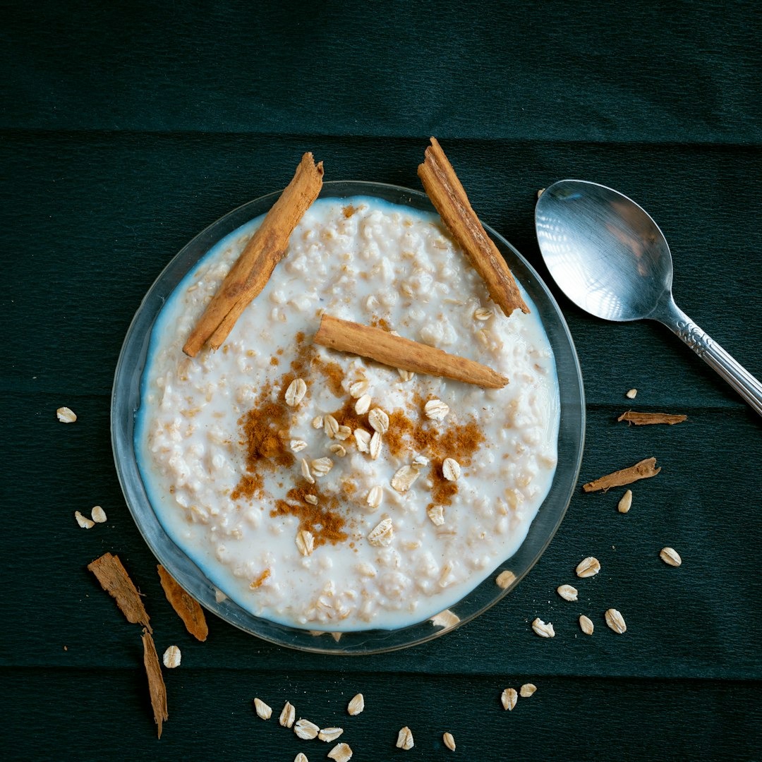 Creamy oatmeal garnished with cinnamon sticks in a glass bowl.