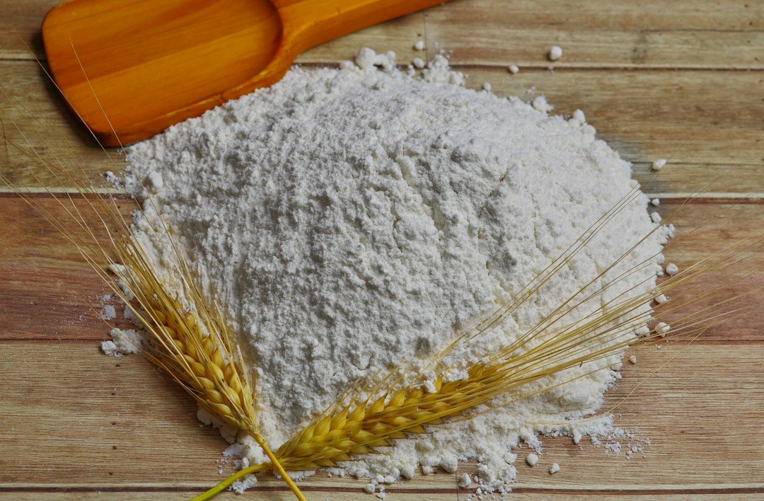 White flour with wheat stalks and a wooden spoon on a wooden table.